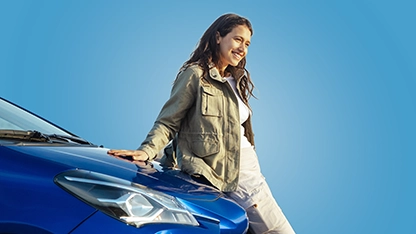 Giovane donna appoggiata a un’auto blu su sfondo azzurro.