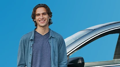 Giovane uomo in camicia azzurra posa accanto a un’auto su sfondo blu