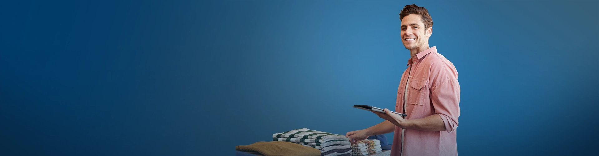 Ragazzo con camicia che tiene in mano un tablet davanti a una pila di maglioni piegati