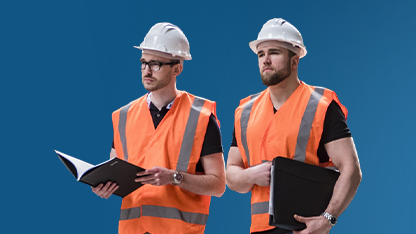 Due uomini in abiti da lavoro posano su uno sfondo blu uniforme. Entrambi indossano caschi protettivi bianchi e giubbotti di sicurezza arancioni ad alta visibilità con strisce catarifrangenti. L'uomo a sinistra ha la barba e tiene una cartellina nera sotto il braccio, mentre l'uomo a destra porta gli occhiali e tiene una cartellina nera tra le mani. Entrambi guardano verso la loro destra con espressione seria.