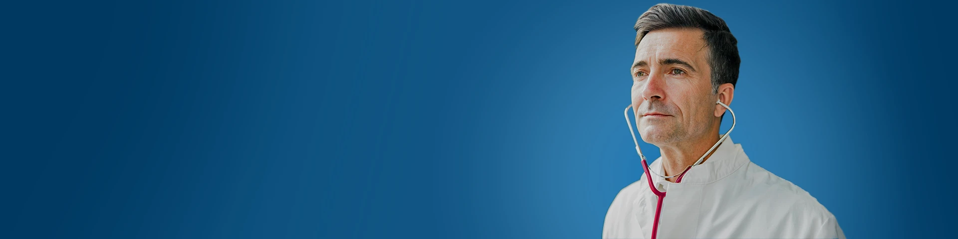 Primo piano di un medico di mezza età con camice bianco, colto di profilo mentre indossa uno stetoscopio e guarda pensieroso verso l'esterno. Lo sfondo è di un blu intenso uniforme. 