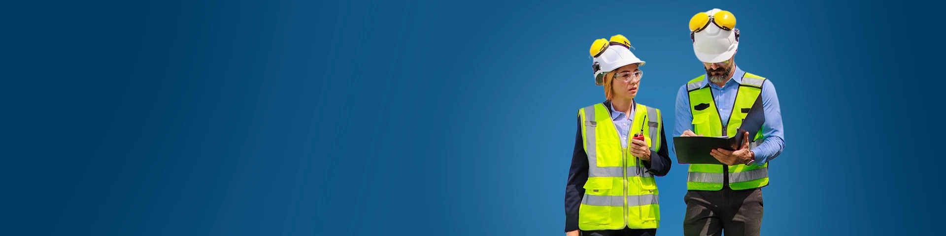 Due ingegneri, un uomo e una donna, in piedi fianco a fianco su uno sfondo blu solido. Entrambi indossano caschi bianchi con paraorecchie protettivi gialli e giubbotti di sicurezza giallo-verdi riflettenti. La donna, a sinistra, guarda verso l'alto con un'espressione pensierosa, tenendo una radio bidirezionale in mano. L'uomo, a destra, guarda in basso mentre scrive o esamina dei documenti su una cartellina nera. L'illuminazione è luminosa e uniforme.