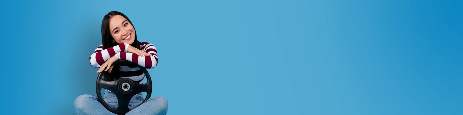 Donna sorridente seduta a gambe incrociate con le braccia appoggiate su un volante