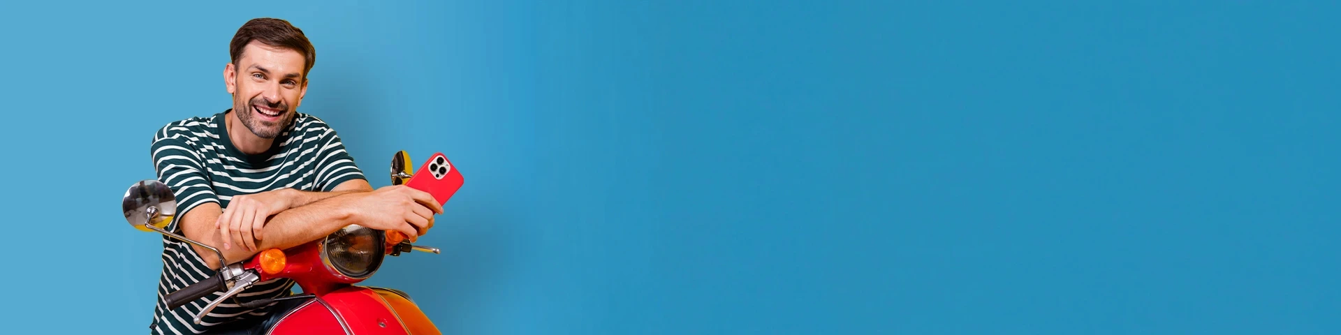 Uomo sorridente appoggiato su un motociclo Vespa con in mano uno smartphone