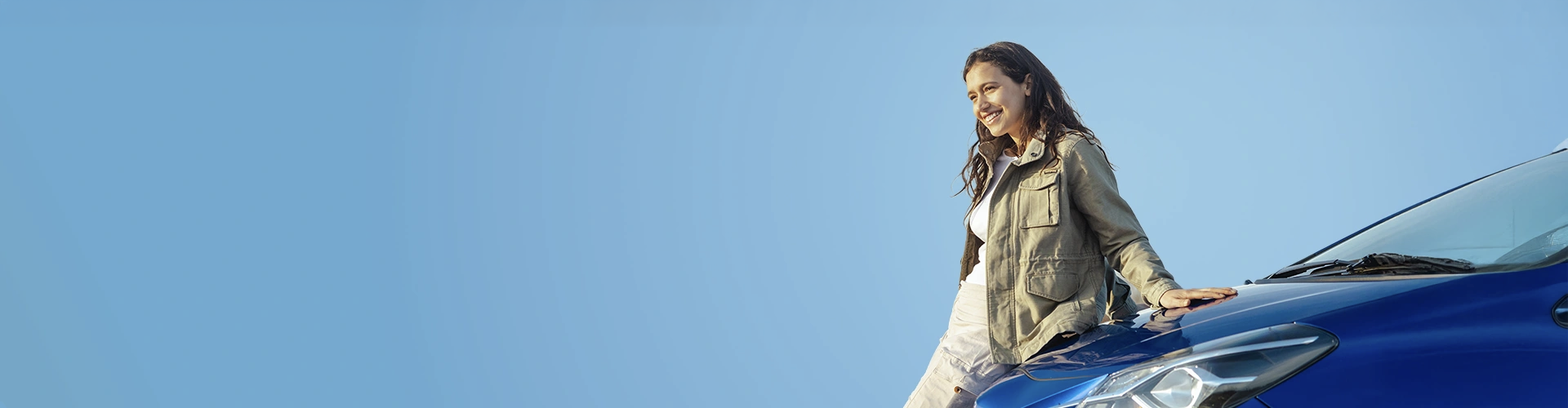 Donna sorridente appoggiata con una mano al cofano della macchina