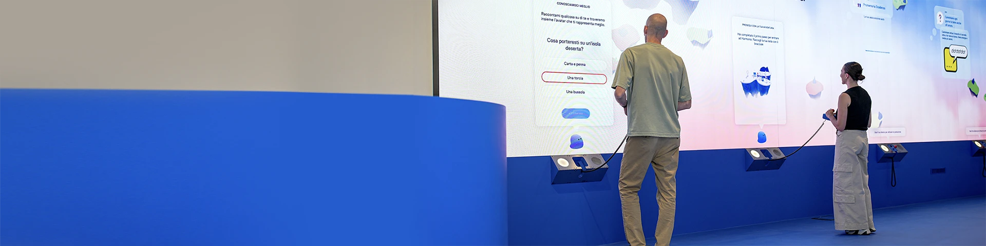 Un uomo e una donna di spalle che interagiscono con un telecomando su un pannello a muro all'interno di AreaX.